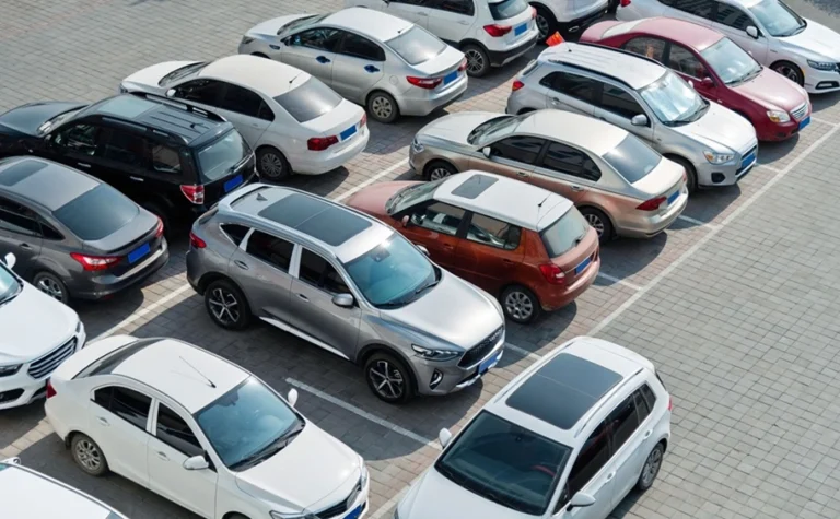 Automobilių stovėjimo aikštelė iš viršaus su tvarkingai priparkuotais įvairių spalvų moderniais lengvaisiais automobiliais ir visureigiais.