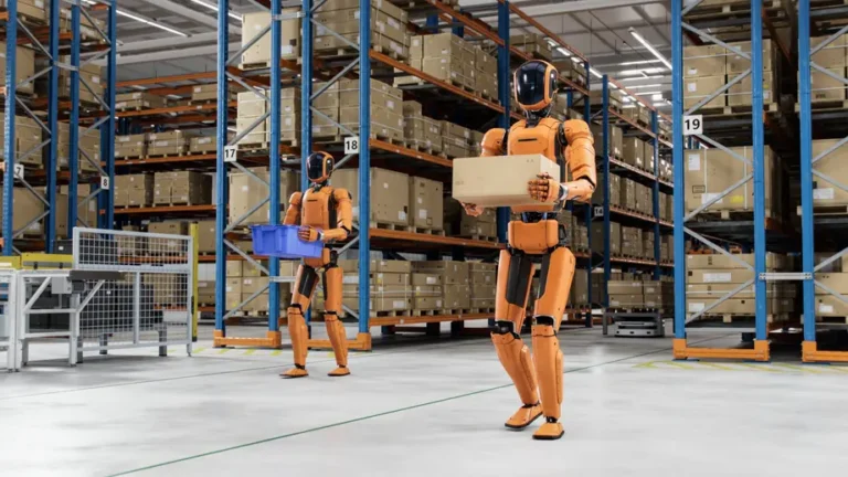 Modernus sandėlis su aukštomis lentynomis, kuriame dirba du oranžinės spalvos robotai. Vienas robotas priekyje neša kartoninę dėžę, kitas fone - mėlyną plastikinę dėžę. Vaizduojama logistikos automatizacija.